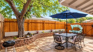 A patio with a table and chairs, a barbecue grill, and a wooden fence.