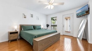 Una camera da letto con un letto, comodini, una ventola a soffitto, una TV e una porta che dà su un balcone.
