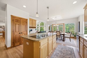 A modern kitchen with wooden cabinets, a granite countertop, and a dining area with a table and chairs. - Washougal 4BR - Hot Tub, Sauna, Private 5 Acres (Washougal)