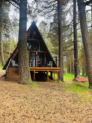 En stuga med en träfasad, stora fönster och en veranda med stolar.