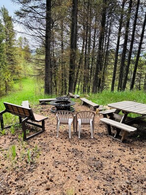 Ett skogsområde med picknickbord och stolar, en eldstad och en bänk.