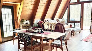 Una habitación con techos altos de madera, una mesa de comedor con sillas, un sofá y un ventanal grande.
