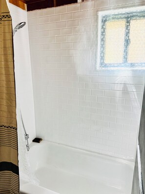 Ein Badezimmer mit weißen Fliesen, einer Dusche und einem Fenster mit dekorativem Rahmen.