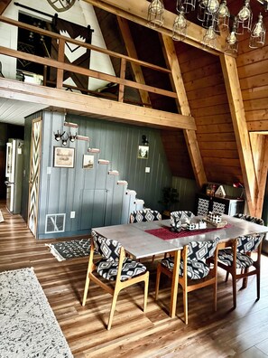 A dining area with a high ceiling and exposed beams, featuring a wooden table and patterned chairs.