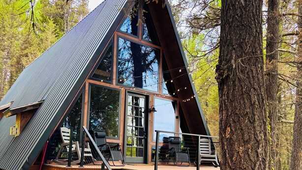 Una cabaña con techo inclinado, ventanas grandes y una terraza de madera con escaleras que conducen a la entrada.