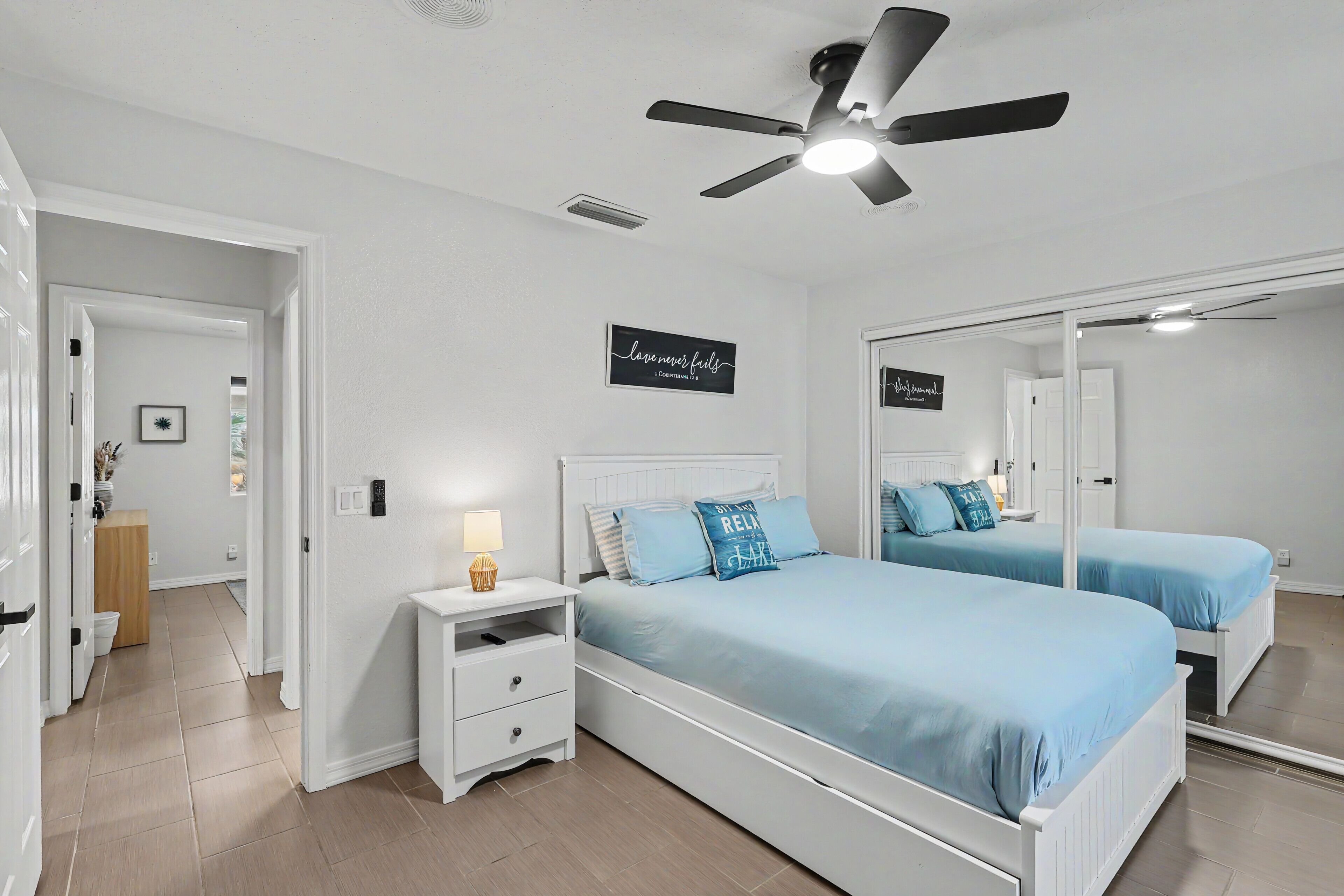 Une chambre avec deux lits, un ventilateur de plafond, une table de chevet avec une lampe et un miroir.