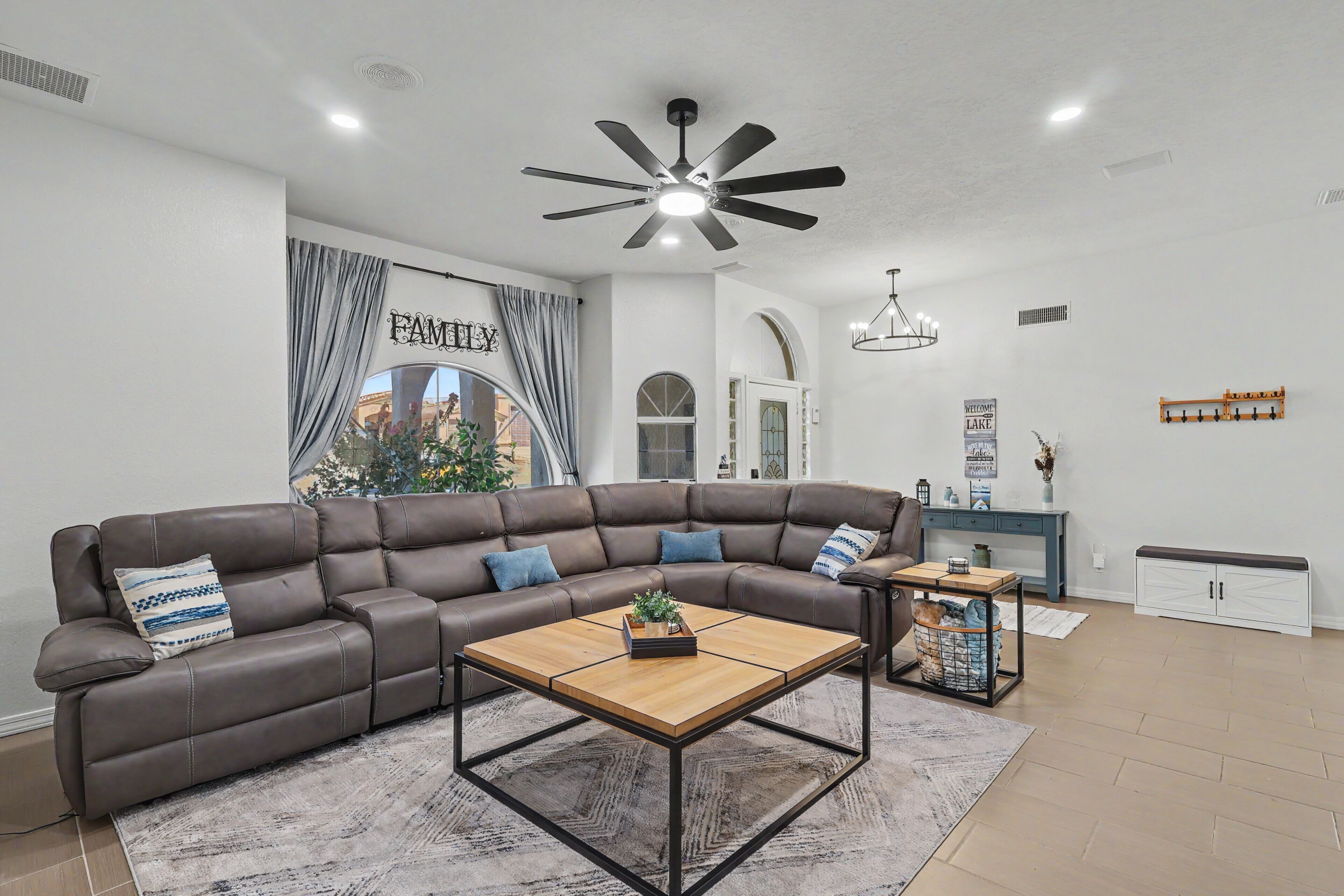 Un salon moderne avec un canapé d’angle, une table basse, un ventilateur de plafond et une vue sur l’extérieur.