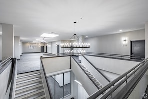 Hotelinterieur met meerdere niveaus, een centraal hanglamp en een trap, met een deur waarop het nummer 210 staat.
