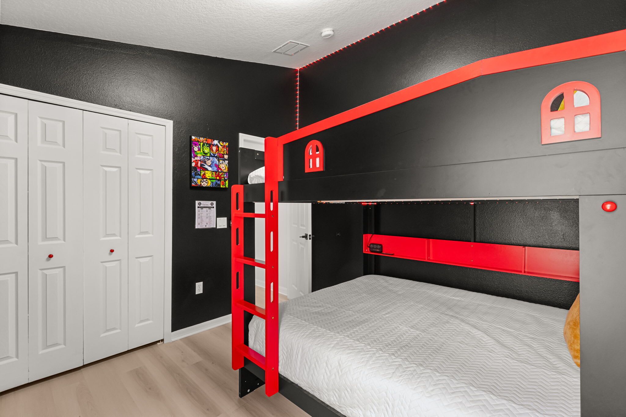 Una cama individual superpuesta con una escalera roja, una puerta blanca y una pared negra y roja con una ventana.