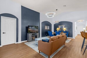 A modern living room with a fireplace, blue chairs, a brown sofa, and a dining area with a table and chairs. - Private Screened Pool | Sleeps 14 | Themed Bunks, Ping Pong & No Rear Neighbors (Davenport)