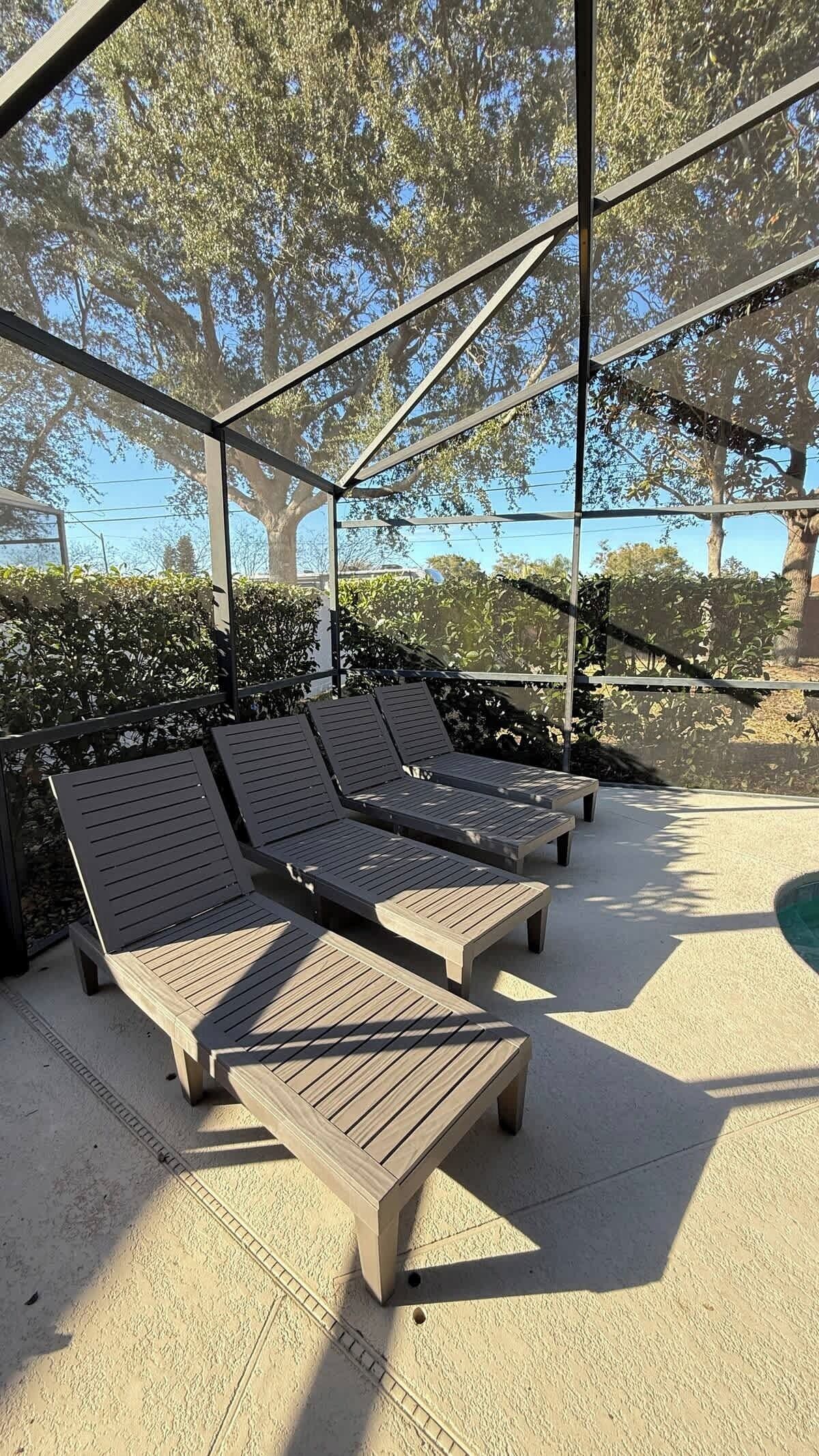 A covered outdoor seating area with wooden lounge chairs and a concrete floor.