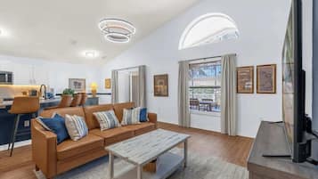 A modern living room with a sofa, coffee table, and TV. There is a kitchen area in the background.