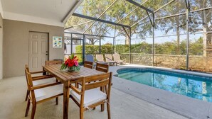 Un espace extérieur abrité comprenant une piscine, une table et des chaises en bois, ainsi qu’un ventilateur de plafond.
