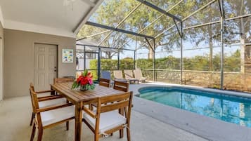 A covered outdoor area with a pool, wooden table and chairs, and a ceiling fan.