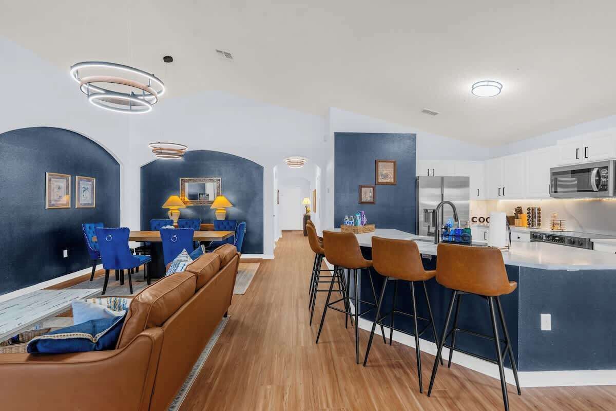 A modern kitchen with a central island, bar stools, and a dining area with blue chairs.