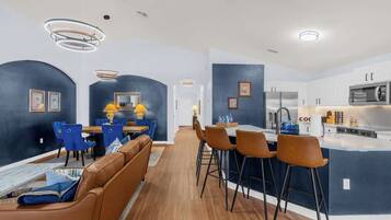 A modern kitchen with a central island, bar stools, and a dining area with blue chairs.