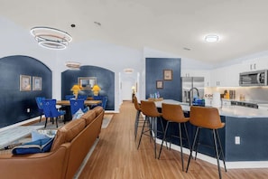 Eine moderne Küche mit einer zentralen Kochinsel, Barhocker und einem Essbereich mit blauen Stühlen.