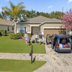 A family walking towards a house with a garage and a mailbox in the driveway. - Private Screened Pool | Sleeps 14 | Themed Bunks, Ping Pong & No Rear Neighbors (Davenport)