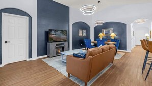 Un salon moderne avec une cheminée, un canapé, un coin repas avec des chaises et un téléviseur.