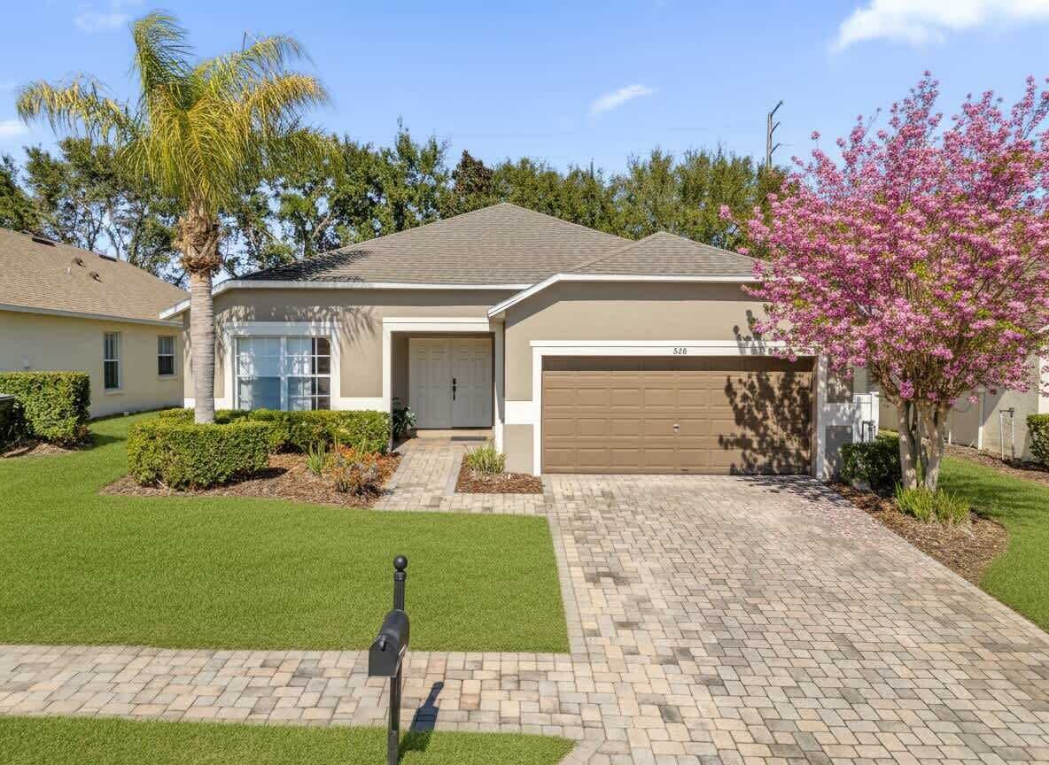 A single-story house with a garage, a well-maintained lawn, and a tree with pink blossoms.