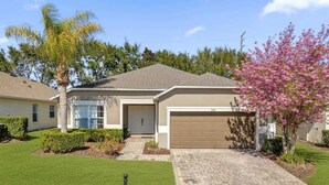 Une maison de plain-pied avec un garage, une pelouse bien entretenue et un arbre aux fleurs roses.