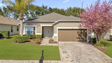 A single-story house with a garage, a well-maintained lawn, and a tree with pink blossoms.