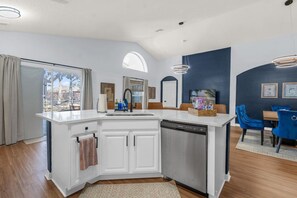A modern kitchen with a dishwasher, a sink, and a dining area with blue chairs. - Private Screened Pool | Sleeps 14 | Themed Bunks, Ping Pong & No Rear Neighbors (Davenport)