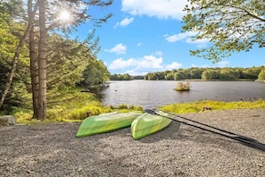 Ein Kiesweg führt zu einem ruhigen See mit Kajaks und einem Paddel.