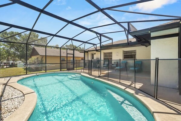 A swimming pool with a clear view of the surrounding area, including a house and a fenced deck.