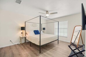 A four-poster bed with a ceiling fan, bedside lamps, and a window with blinds.