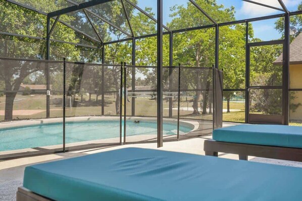 Une piscine extérieure couverte, dotée d’une structure en verre, de bancs et offrant une vue sur des arbres et un bâtiment en arrière-plan.