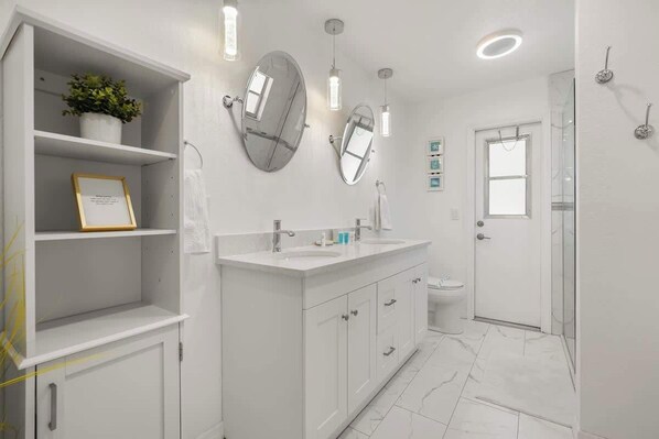 A modern bathroom with a white vanity, two mirrors, a shower, and a toilet.