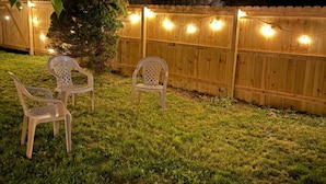 A backyard with a wooden fence, string lights, and two white plastic chairs. - The Retro Nook - cozy studio near Spooky Nook. (Hamilton)