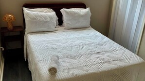A neatly made bed with a white quilt, a wooden headboard, and a nightstand with a lamp. - The Retro Nook - cozy studio near Spooky Nook. (Hamilton)