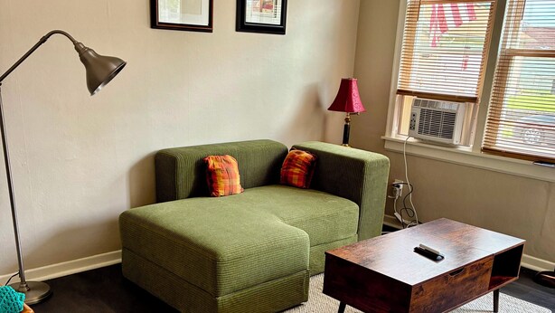 A living room with a green sofa, a wooden coffee table, a floor lamp, and a window with blinds. - The Retro Nook - cozy studio near Spooky Nook. (Hamilton)