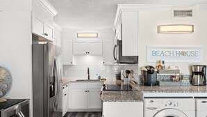 A kitchen with white cabinets, a stainless steel refrigerator, a coffee maker, and a washing machine. - The Summit 518 - Beach Front, 2 Pools, & Hot Tubs (Panama City Beach)