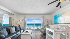A living room with a sofa, coffee table, dining table, and chairs. There is a large window with a view of the beach and ocean. - The Summit 518 - Beach Front, 2 Pools, & Hot Tubs (Panama City Beach)