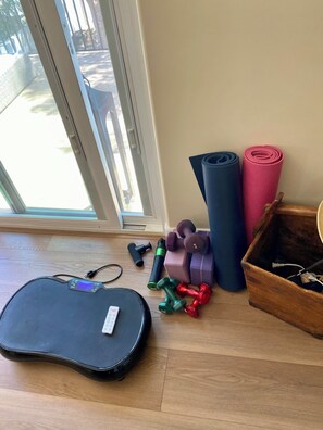 Ein Zimmer mit einer Schiebeglastür, einer Yogamatte, Kurzhanteln, einer Kettlebell und einem Koffer.