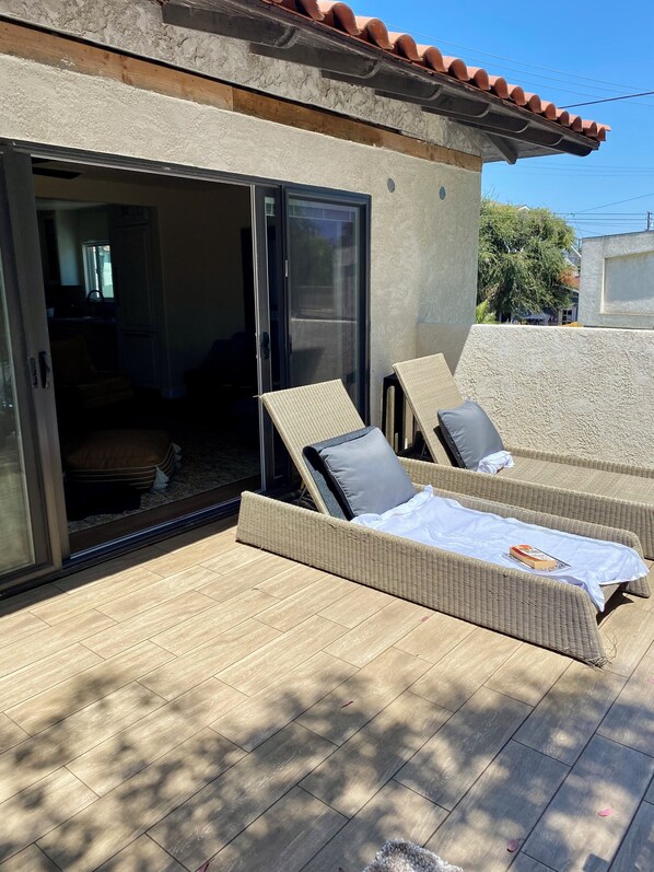 A sunlit outdoor lounge area with wicker furniture and a sliding glass door leading to an interior space.