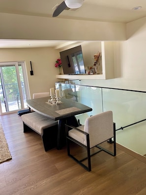 A modern dining area with a glass partition, a flat-screen TV mounted above the table, and a bench. - Upscale, Family Friendly Coastal Retreat.
2 Blocks from So Cal’s, Seal Beach (Seal Beach)