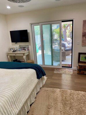 A bedroom with a bed, a TV, a desk, and a sliding glass door leading to an outdoor area.