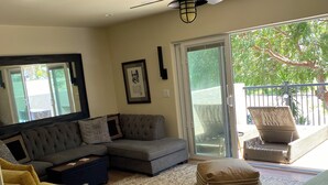 A living room with a sectional sofa, a yellow armchair, a glass coffee table, a ceiling fan, and a view through a sliding glass door to an outdoor area. - Upscale, Family Friendly Coastal Retreat.
2 Blocks from So Cal’s, Seal Beach (Seal Beach)