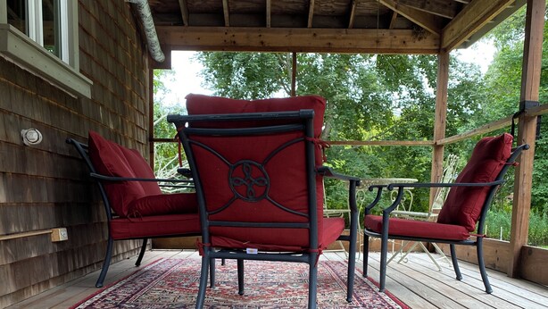 Una terraza de madera con dos sillones tapizados en rojo y una pequeña mesa, todo ello rodeado por una barandilla de madera.