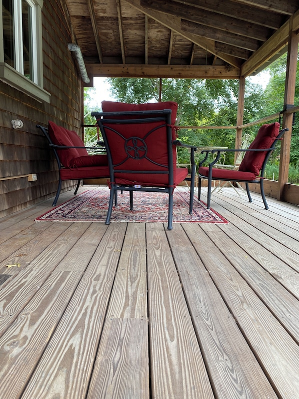 A wooden deck with two red upholstered chairs and a small table, surrounded by a wooden railing.