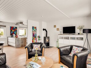Een moderne woonkamer met leren banken, een salontafel, een open haard, een televisie en een keukenhoek met een witte bakstenen muur.
