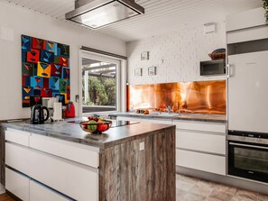Una cocina moderna con armarios blancos, una isla de madera, un cuadro abstracto colorido y vistas a través de la ventana.