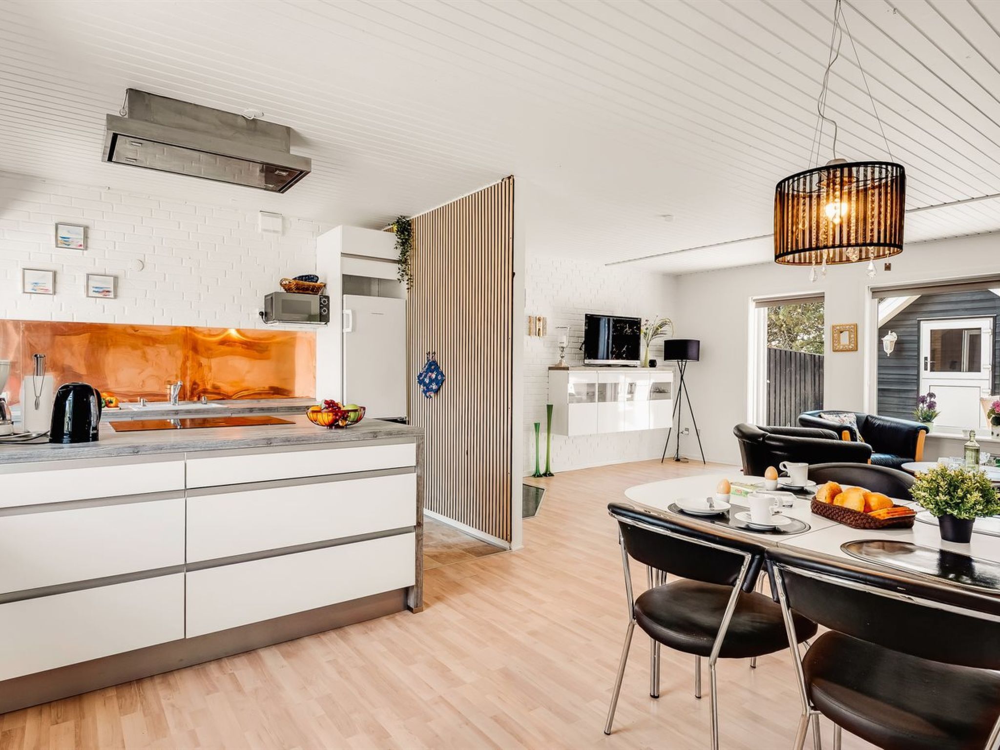 Une cuisine moderne avec des meubles blancs, un îlot central en bois et un coin repas comprenant une table et des chaises en cuir noir.