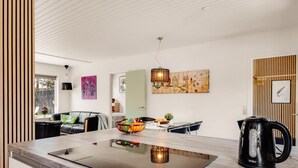 Eine moderne Küche mit einer Kochinsel, einem Essbereich mit Tisch und Stühlen sowie ein Wohnbereich mit Sofa und Gemälde.