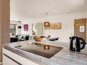 Een moderne keuken met een centraal eiland, een zithoek met een tafel en stoelen, en een woongedeelte met een bank en een schilderij.