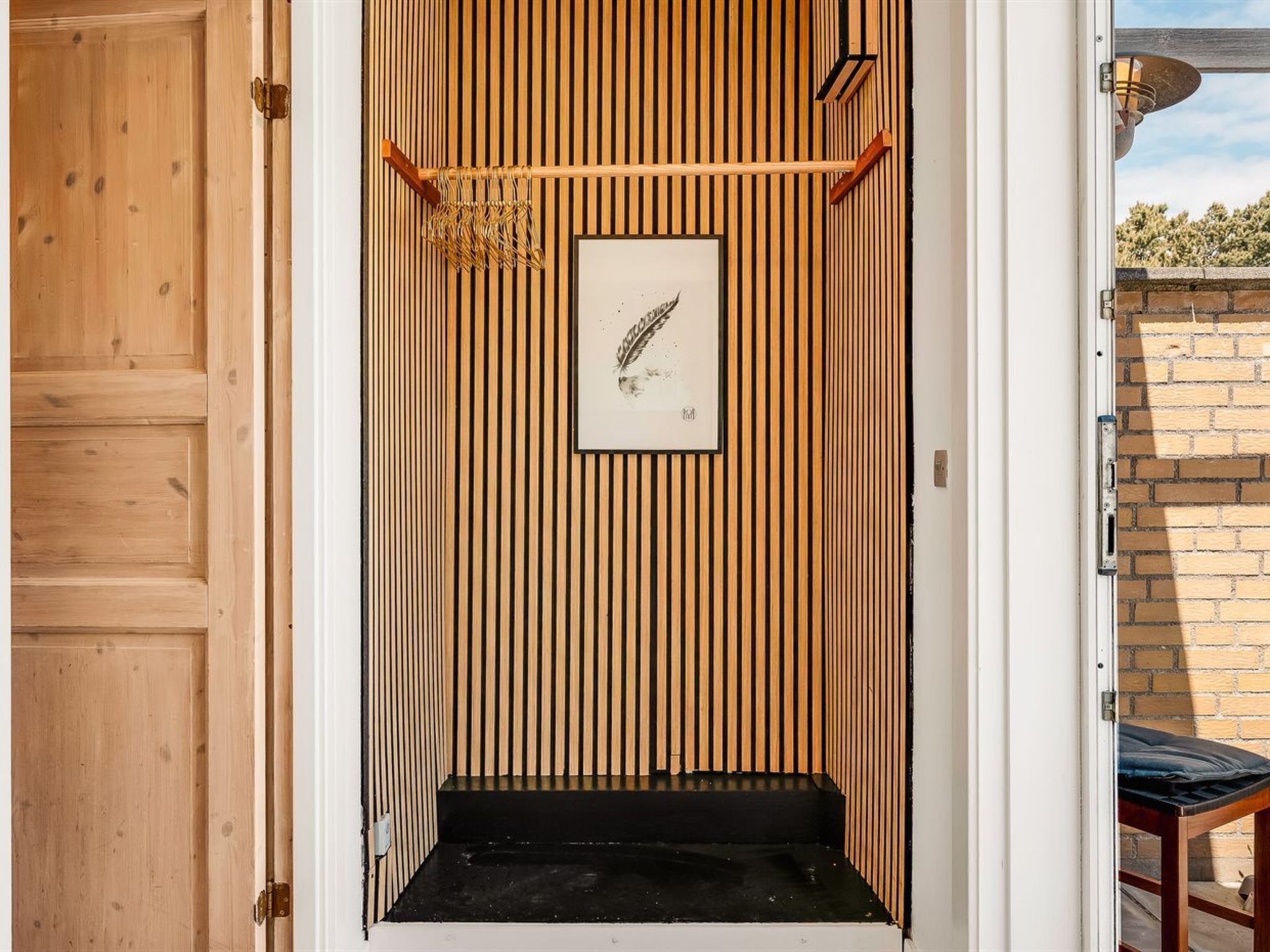 Una habitación con listones verticales de madera, un cuadro en la pared y un banco negro en la entrada.
